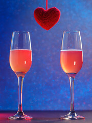two glasses of champagne and a red knitted heart, bokeh blue or neon background. Vertical photo