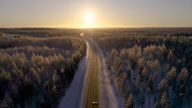 Aerial view of cargo truck on road driving towards golden sunset in winter in nordic country. Freight transportation concept.