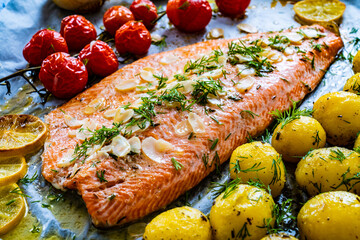 One sheet pan Roast trout fillet with potatoes and vegetable salad served on black stone plate on wooden table
