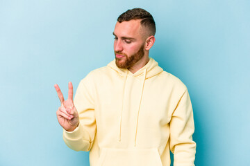 Fototapeta premium Young caucasian man isolated on blue background joyful and carefree showing a peace symbol with fingers.
