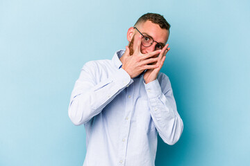 Young caucasian man isolated on blue background blink through fingers frightened and nervous.