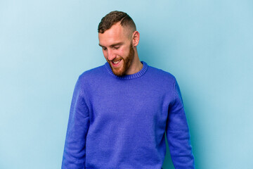 Fototapeta premium Young caucasian man isolated on blue background laughs and closes eyes, feels relaxed and happy.