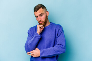 Young caucasian man isolated on blue background thinking and looking up, being reflective, contemplating, having a fantasy.