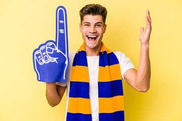 Young sports fan man isolated on yellow background receiving a pleasant surprise, excited and raising hands.