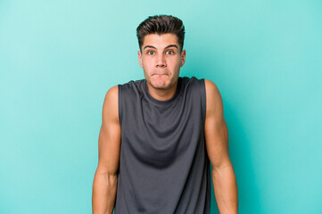 Young caucasian man isolated on blue background shrugs shoulders and open eyes confused.