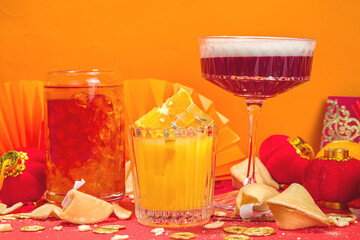 Chinese New Year Cocktail drinks, set of three different glass with various red gold color alcohol party beverage, with traditional Chinese New Year decor, greeting envelopes, Chinese lanterns, coins