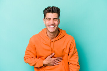 Young caucasian man isolated on blue background laughs out loudly keeping hand on chest.
