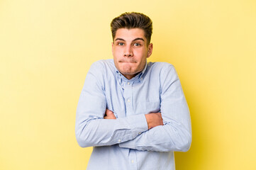 Young caucasian man isolated on yellow background shrugs shoulders and open eyes confused.