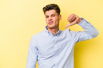 Young caucasian man isolated on yellow background showing a dislike gesture, thumbs down....