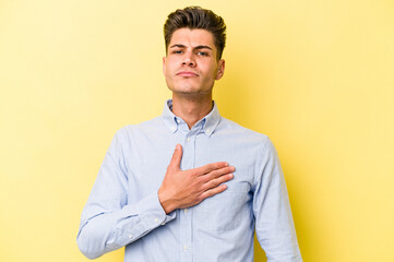 Young caucasian man isolated on yellow background taking an oath, putting hand on chest.