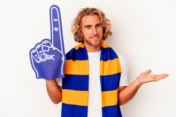 Young sports caucasian fan man isolated on white background showing a copy space on a palm and holding another hand on waist.