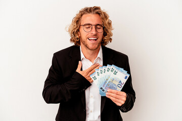 Young caucasian business man holding banknotes isolated on white background laughs out loudly keeping hand on chest.