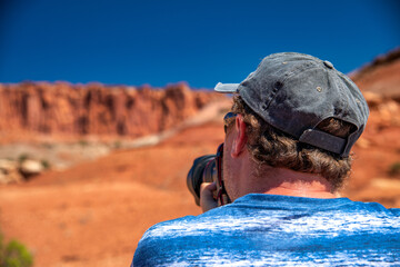 Male Photographer in Capitol Reef National Park, Utah. Red rocks under a blue summer sky.