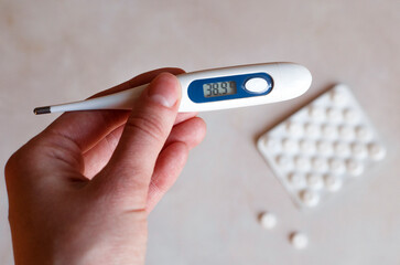 Keep a thermometer with a high temperature in your hand. On a light background is a package of pills