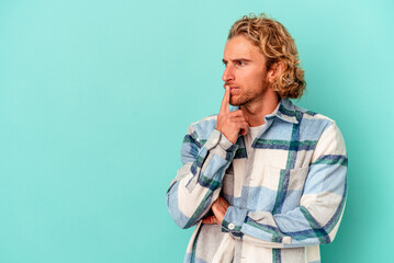 Young caucasian man isolated on blue background looking sideways with doubtful and skeptical expression.