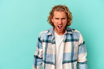 Young caucasian man isolated on blue background shouting very angry, rage concept, frustrated.