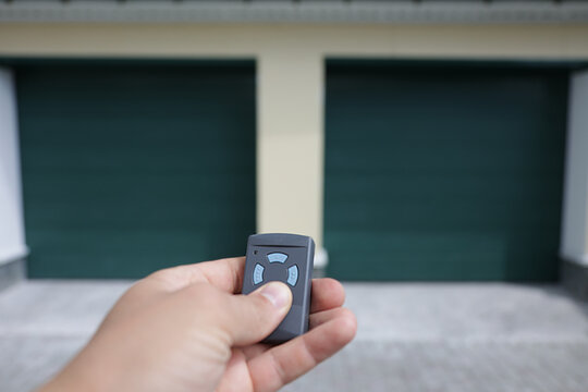 The Man Holds In His Hand A Remote Control That Opens The Door Of A Double Garage. A Convenient Key For Opening The Garage Door.