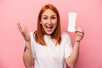 Fototapeta Young caucasian woman holding sanitary napkin isolated on pink background receiving a pleasant surprise, excited and raising hands. obraz