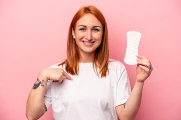 Young caucasian woman holding sanitary napkin isolated on pink background person pointing by hand to a shirt copy space, proud and confident
