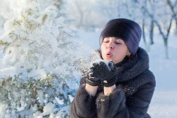 An adult woman blows fluffy snow off her gloves on frosty sunny day,