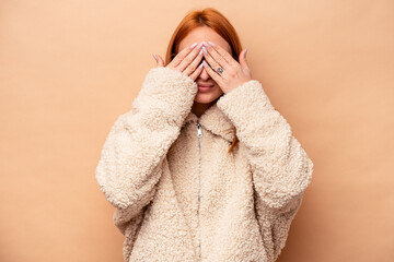 Young caucasian woman isolated on beige background afraid covering eyes with hands.