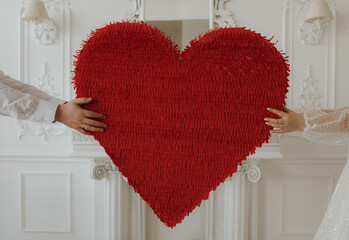 A young husband and wife hold a big red heart with their hands.