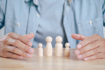 The man Hands protect over wooden peg dolls. planning, saving family,  health care and insurance, family mental health, international day of families.
