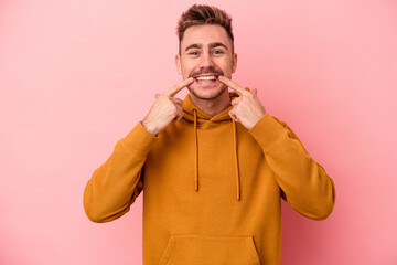 Young caucasian man isolated on pink background smiles, pointing fingers at mouth.