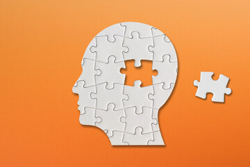 Brain shaped white jigsaw puzzle on orange background, a missing piece of the brain puzzle, mental...