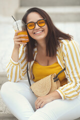 Happy plus size girl holding a cold take away orange drink in hands and enjoying the summer day in city park. Close-up portrait of beautiful stylish curvy woman 30 yeasr old having fun and smiling 