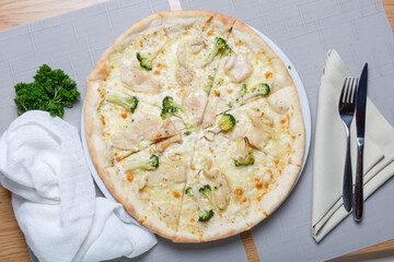 Pizza with chicken and broccoli on a white plate with a knife and fork