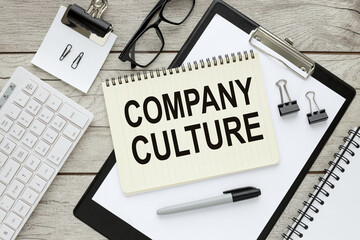 Company Culture text on open notepad on black folder on wooden table near keyboard