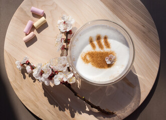 Blooming spring branch near a cup of coffee with a pattern of cinnamon on milk foam on a round wooden stand. view from above. Positive thinking, good morning, hello spring. sunny day
