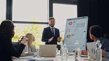 smiling man talking near flipchart during business meeting with interracial colleagues