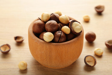 Peeled macadamia nuts in wooden bowl on light background.