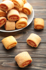 Homemade cookies, mini rolls with apricot jam in plate on brown wooden background. Vertical photo.