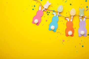 Easter bunnies handmade from colored paper on a rope with clothespins easy crafts for children on yellow background.
