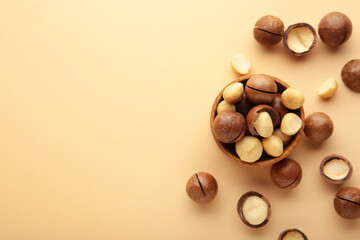 Peeled macadamia nuts in wooden bowl on beige background.