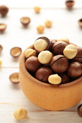 Peeled macadamia nuts in wooden bowl on white background. Vertical photo