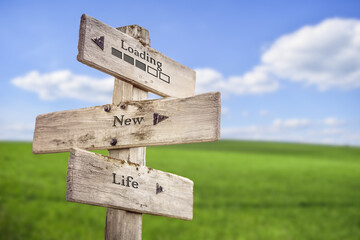 Loading text and bar with new life text quote engraved on wooden signpost outdoors on green field with blue sky.