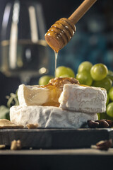 Organic homemade camembert or brie cheese on a wooden board with grapes and nuts and honey.