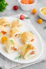 Thin pancake rolls or crepes rolls with smoked salmon, cream cheese, cucumber and dill on a gray concrete background. Selective focus.