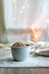 Plate with almond chocolate bar, mug with chocolate chip cookies, open book, reading glasses, soft blanket and lit candles. Hygge at home. Selective focus.