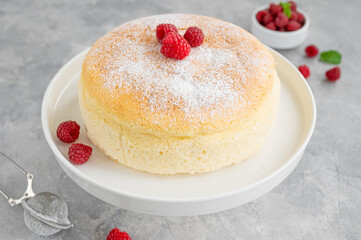 Japanese cotton cheesecake on a stand on a gray concrete background with fresh raspberries and powdered sugar on top. Selective focus, copy space.