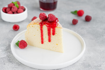 Japanese cotton cheesecake on a stand on a gray concrete background with fresh raspberries and powdered sugar on top. Selective focus, copy space.