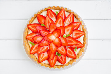 Strawberry tart with custard cream on a plate on a white wooden background. Copy space.