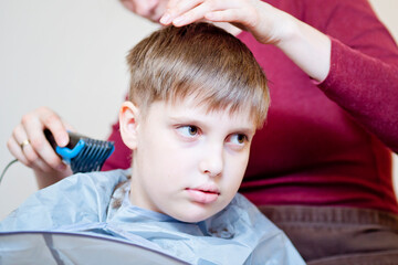 Hairdressing saloon at home in quarantine conditions. Mother cuts boy's hair with scissors.