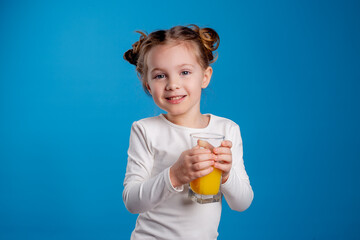 little girl with a funny hairstyle in a white T-shirt holds a glass with juice in her hands. blue background. useful products for children. space for text. High quality photo