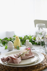 Easter table setting with yellow chick, festive decorations, fresh flowers and eggs. Elegance dinner at home interior. Close up.