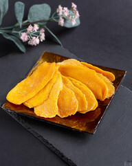 A few pieces of dried mango on a square glass plate on a black background. Healthy desserts, vegetarianism, healthy food concept